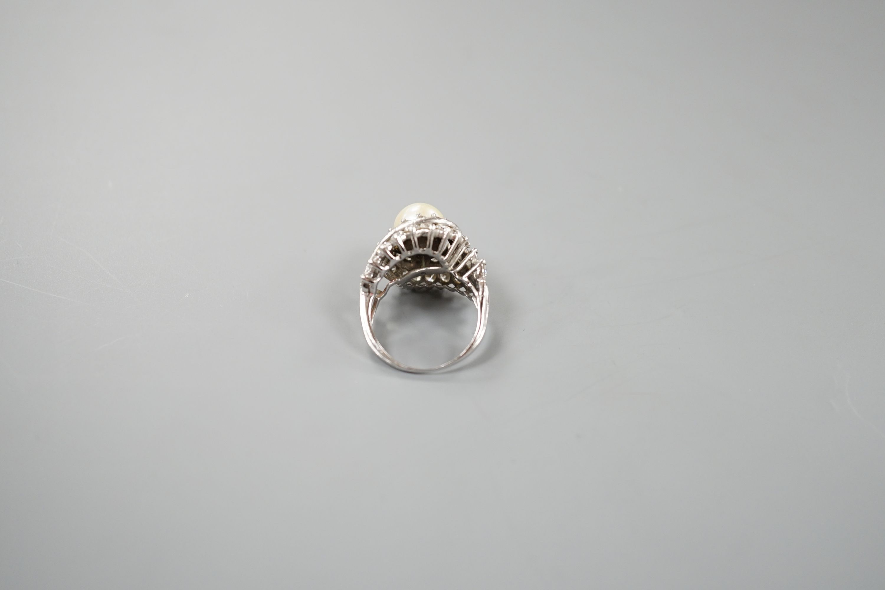 A white metal single stone cultured pearl and diamond cluster set scroll dress ring, size Q, gross weight 13.6 grams.